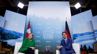 Le PM Trudeau et la chancelière Merkel s'assoient et regardent les caméras.