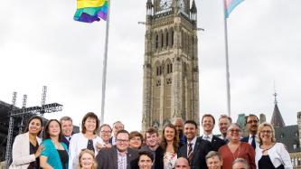 PM Trudeau and MPs pose for a photo in front of the pride and trans flags
