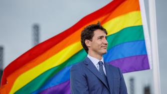 PM Trudeau stands in front of the Pride flag