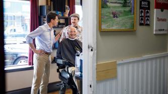 PM Trudeau speaks with a barber and a man in a barber’s chair
