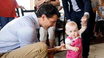 PM Trudeau holds the arm of a toddler while others look on