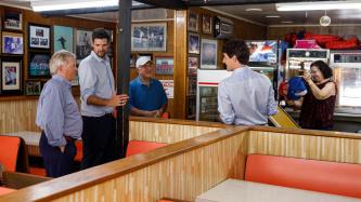 PM Trudeau leans on a pizzeria booth looking toward three others