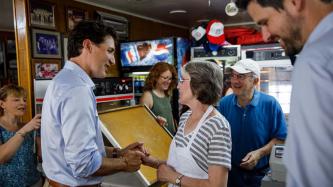 PM Trudeau shakes hands with a woman inside a pizzeria