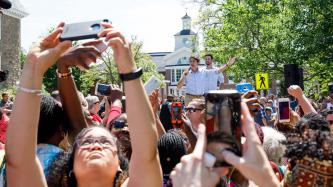 PM Trudeau gestures with mic in hand among a large outdoor crowd
