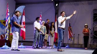 PM Trudeau stands at center stage holding a mic
