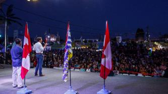 PM Trudeau holds a mic on stage while facing a large crowd