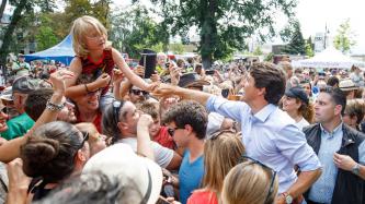 PM Trudeau shakes hands with a little girl in a large crowd