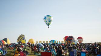 A group of spectators watch hot air balloons flying in the sky