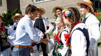 PM Trudeau shakes hands with a young girl in traditional Polish dress