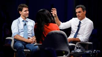 President Sánchez speaks to the moderator while PM Trudeau looks on