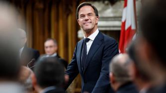 PM Rutte stands and smiles in the House of Commons
