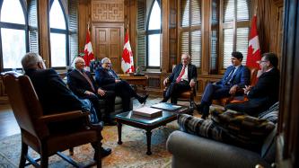 PM Trudeau and Mr. Jean Chretien sit with others in an office