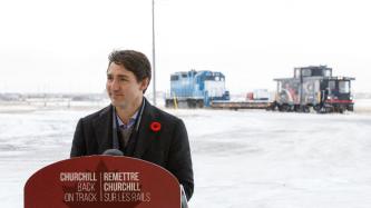 PM Trudeau stands at a podium in front of rail cars