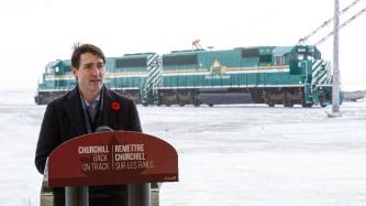 PM Trudeau speaks at a podium in front of a green train