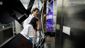 A woman operates lab equipment while PM Trudeau looks on