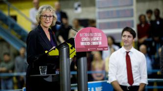 MP Murray speaks at a podium while PM Trudeau look on