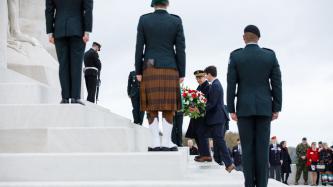 PM Trudeau carries flowers up the stairs of the monument while military personnel look on