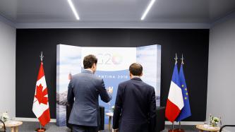 PM Trudeau and President Macron talk while heading towards their chairs