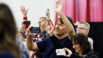 Crowd members take photos and wave
