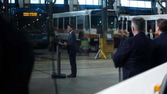 PM Trudeau stands at a podium with buses in the background