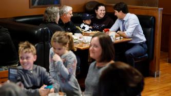 Le PM Trudeau, assis, parle avec une famille dans le restaurant