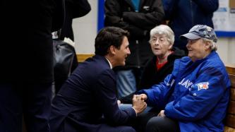 PM Trudeau kneels and shakes hands with a woman