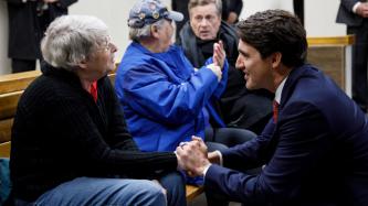 PM Trudeau kneels and shakes hands with a woman