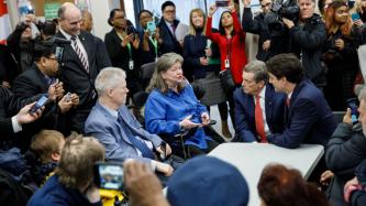PM Trudeau and Mayor Tory sit and talk with a woman in a wheelchair