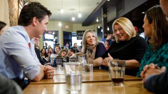 A woman speaks while PM Trudeau and others listen