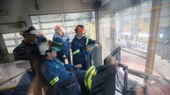 Le PM Trudeau porte des lunettes et un casque de sûreté et discute avec des employés de l’Aluminerie Alouette