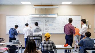 Le PM Trudeau regarde des élèves écrire sur un tableau blanc