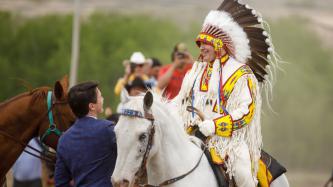Chief Bellegarde, on horseback and wearing a headdress, greets PM Trudeau