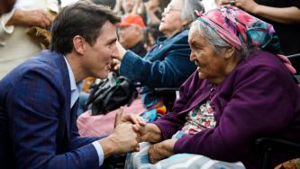 PM Trudeau kneels and shakes hands with an elderly woman