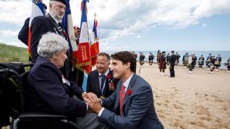PM Trudeau crouches and holds the hands of a veteran