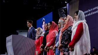 PM Trudeau stands at a podium next to women in veils