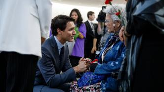 PM Trudeau kneels and speaks to an elderly woman