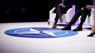 A view of the NATO emblem on a stage floor and the shoes of two seated men