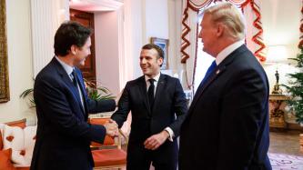 Le PM Trudeau et le président Macron se serrent la main en souriant, sous le regard du président Trump