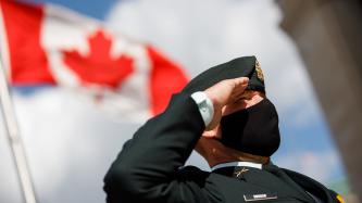 A soldier salutes while standing next to a Canadian flag