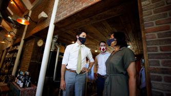 PM Trudeau, MP Amos, and a woman stand inside a brick entrance way