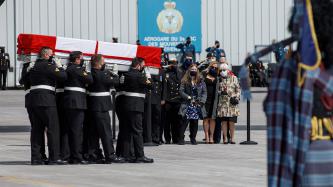 Military pallbearers carry a coffin draped in a Canadian flag
