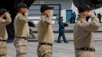 Des militaires en position de salut, un collègue transporte un chapeau de service sur un coussin