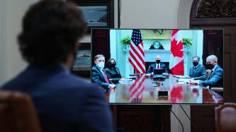 PM Trudeau's profile facing a screen of President Biden and VP Harris and others around a table