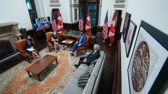 PM Trudeau, DPM Freeland, Minister Garneau and a woman sit with a nearby screen of POTUS team