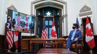 Le PM Trudeau est assis près d’un écran où on peut voir l’équipe du président des États-Unis