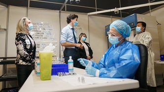 A nurse prepares a doses of vaccine while PM Trudeau talks with others
