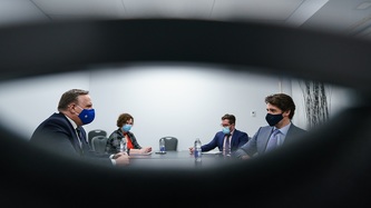 PM Trudeau and PM Legault sit facing each other as a woman and a man look on