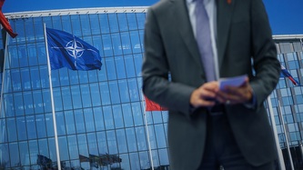 PM Trudeau stands outside in front of the NATO flag