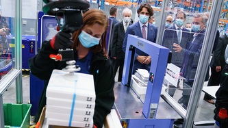 Prime Minister Trudeau looks at an employee manipulating boxes of vaccines