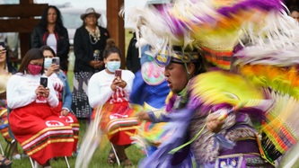 People watch as someone performs a dance in ceremonial attire.